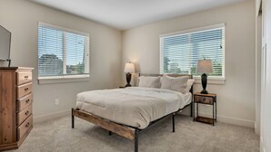 A bedroom with a bed, two bedside tables with lamps, a dresser, and two windows with blinds. - Hill Field 3 by CDH in Layton (Layton)
