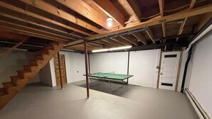 A basement with a ping pong table, wooden stairs, and a door. - Tranquil lodge Ski. Stay. Hike. Soak in the River and Views. (Brookline)