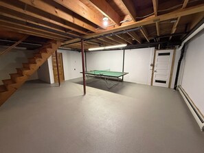 Kælder med et pingpongbord, trætrapper og en dør.