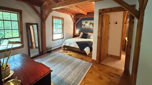 A bedroom with a wooden ceiling, a bed with pillows, a nightstand, a window, and a door. - Tranquil lodge Ski. Stay. Hike. Soak in the River and Views. (Brookline)