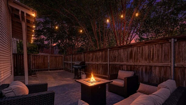 Een terras buiten met rieten meubilair, een vuurkorf en lichtjes.