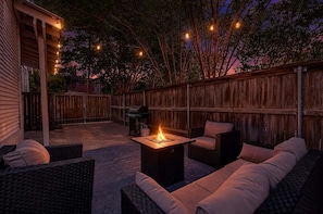 Une terrasse extérieure aménagée avec des meubles en osier, un foyer et des guirlandes lumineuses.