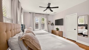 Een slaapkamer met een groot bed, een plafondventilator, een televisie en een deur.