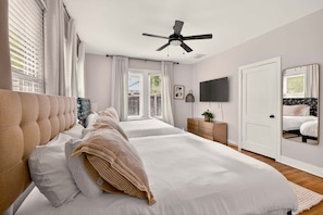 A bedroom with a large bed, a ceiling fan, a TV, and a door.