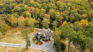 Une grande maison à deux étages, dotée d’une véranda qui fait le tour de la maison, et entourée d’une zone boisée aux couleurs automnales.