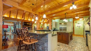 Une cuisine spacieuse dotée d’un îlot central en pierre, de tabourets de bar en bois et d’un grand îlot intégrant une plaque de cuisson.