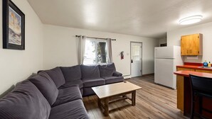A compact living space with a sofa, a small table, a kitchenette with a refrigerator, and a door leading to another room. - Peaceful 1BR Escape Near Glacier National Park (Columbia Falls)