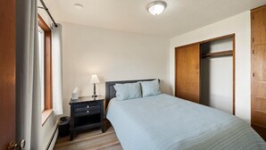 A bedroom with a bed, a nightstand, a lamp, a wooden wardrobe, and a window with curtains. - Peaceful 1BR Escape Near Glacier National Park (Columbia Falls)