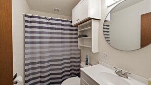 A bathroom with a striped shower curtain, a toilet, a sink with a mirror, and a shelf with toiletries. - Peaceful 1BR Escape Near Glacier National Park (Columbia Falls)