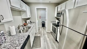 Cozinha moderna com bancadas de granito, eletrodomésticos de aço inoxidável e armários brancos.