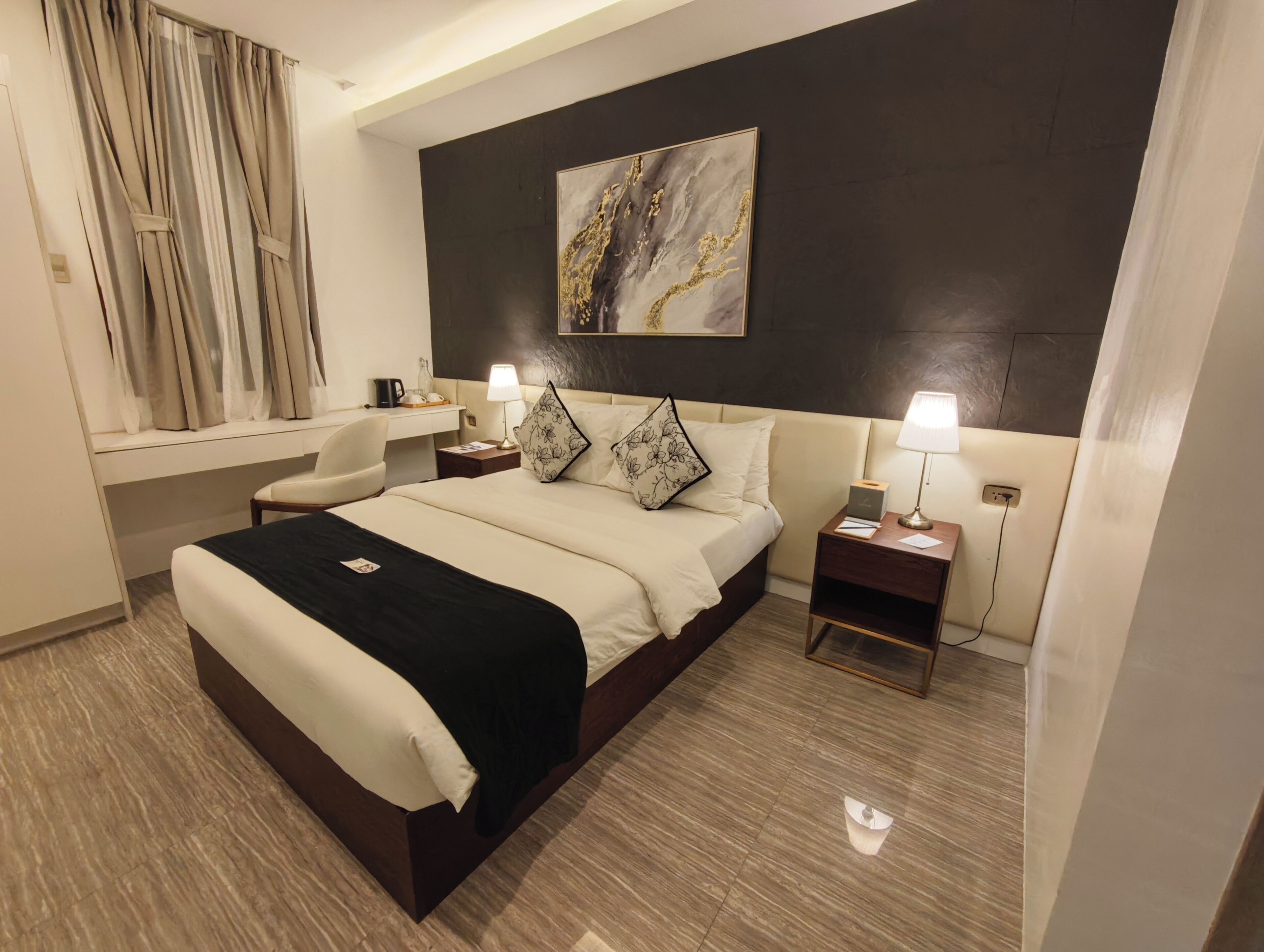 Een moderne hotelkamer met een groot bed, nachtkastjes, een bureau en een raam met gordijnen.