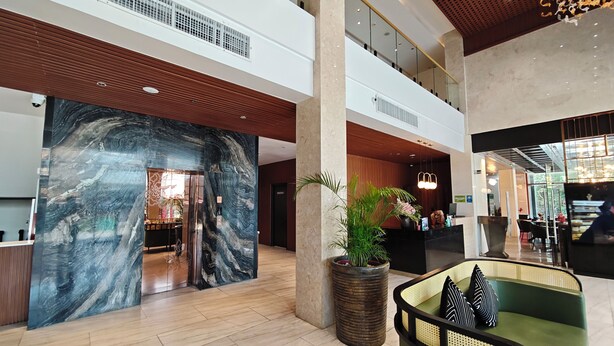 A spacious lobby with a reception desk, a large marble wall, a green sofa, and a potted plant.