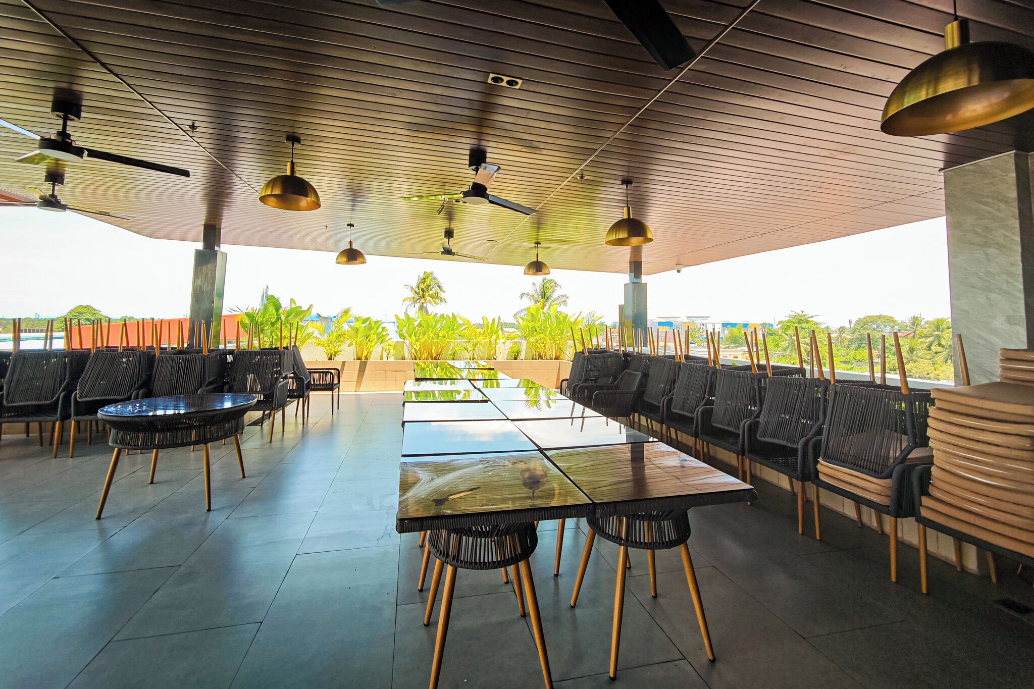 A covered outdoor seating area with tables and chairs, ceiling fans, and a view of greenery.
