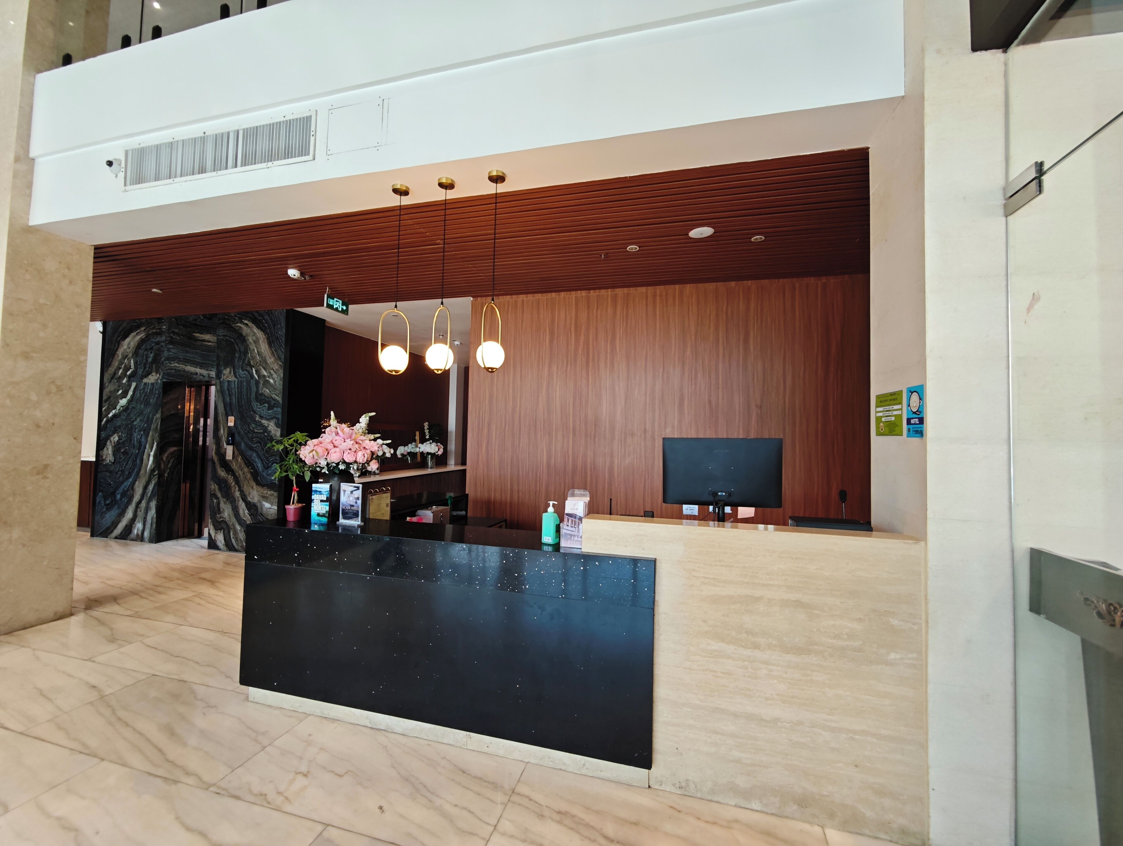 A reception area with a marble floor, a black reception desk, wooden paneling, and a large mirror.