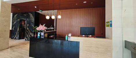 A reception area with a marble floor, a black reception desk, wooden paneling, and a large mirror.