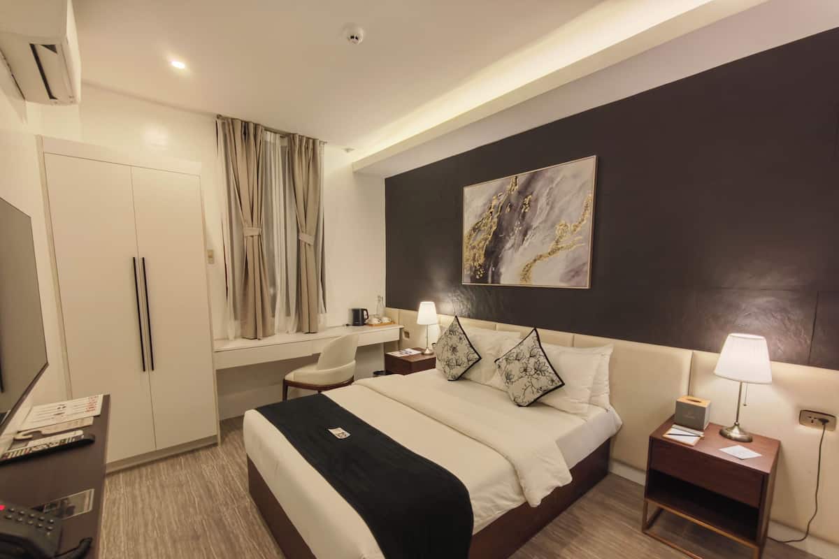 Una habitación de hotel con cama, escritorio, silla, mesitas de noche y un cuadro en la pared.