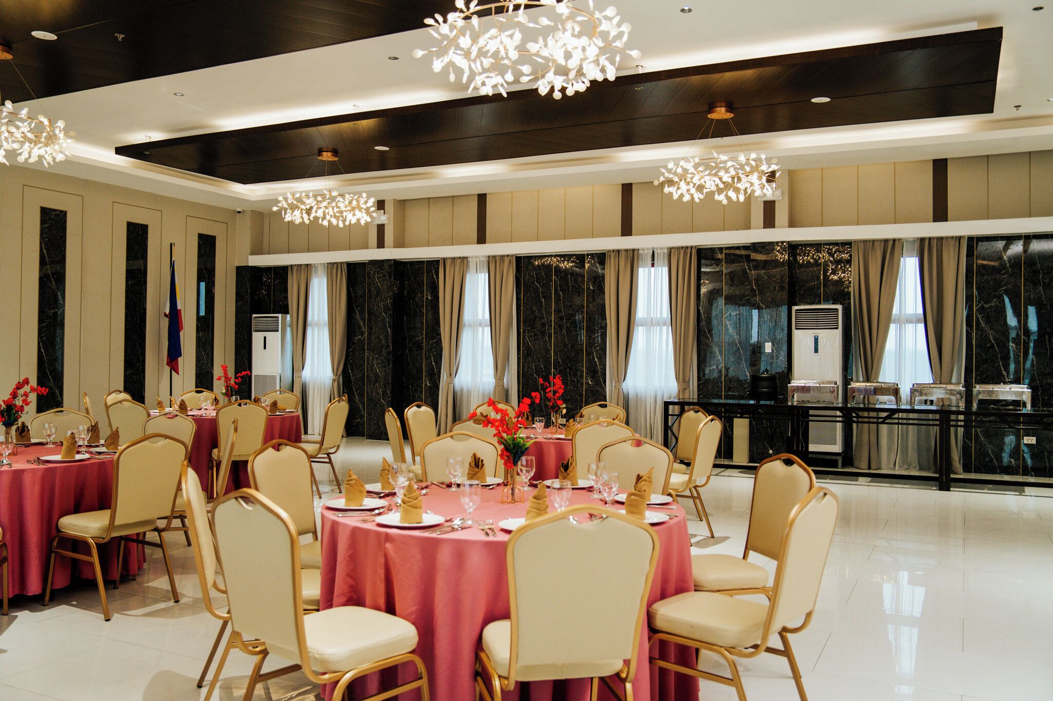 A spacious banquet hall with round tables, chairs, and a large window with curtains.