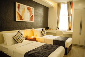 A hotel room with two beds, a desk, a chair, a wardrobe, and artwork on the wall.