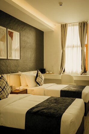 Ein Hotelzimmer mit zwei Betten, einem Schlafsofa, einem kleinen Tisch und einem Fenster mit Vorhängen.