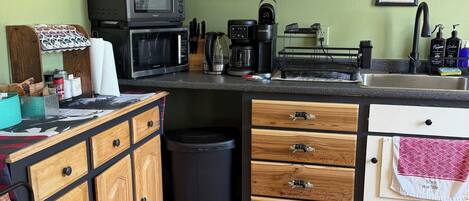 Una cocina compacta con microondas, cafetera y un pequeño cesto de basura.