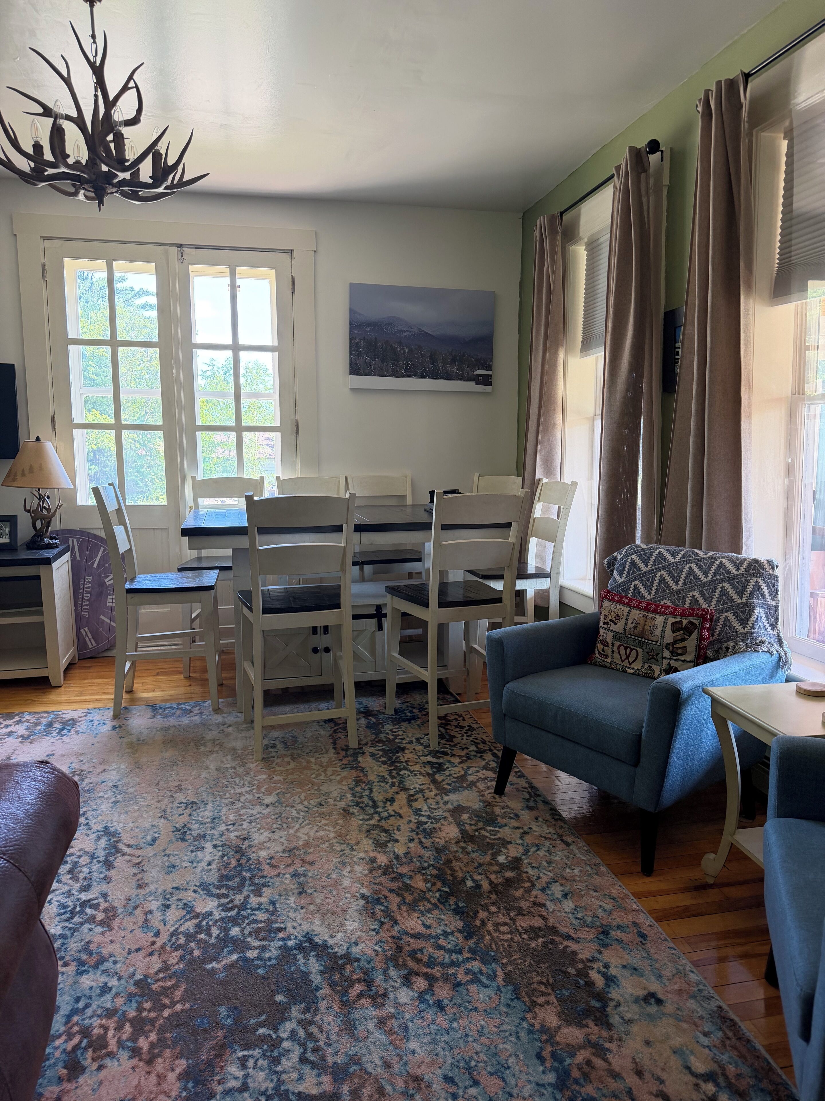 A room with a dining table, chairs, a blue sofa, a patterned rug, and a chandelier.