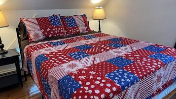A bed with a red, white, and blue quilt, two bedside lamps, and a wooden nightstand.