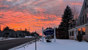 A hotel sign with a mountain silhouette, surrounded by snow-covered trees and a road. - Allegory Inn (Carroll)