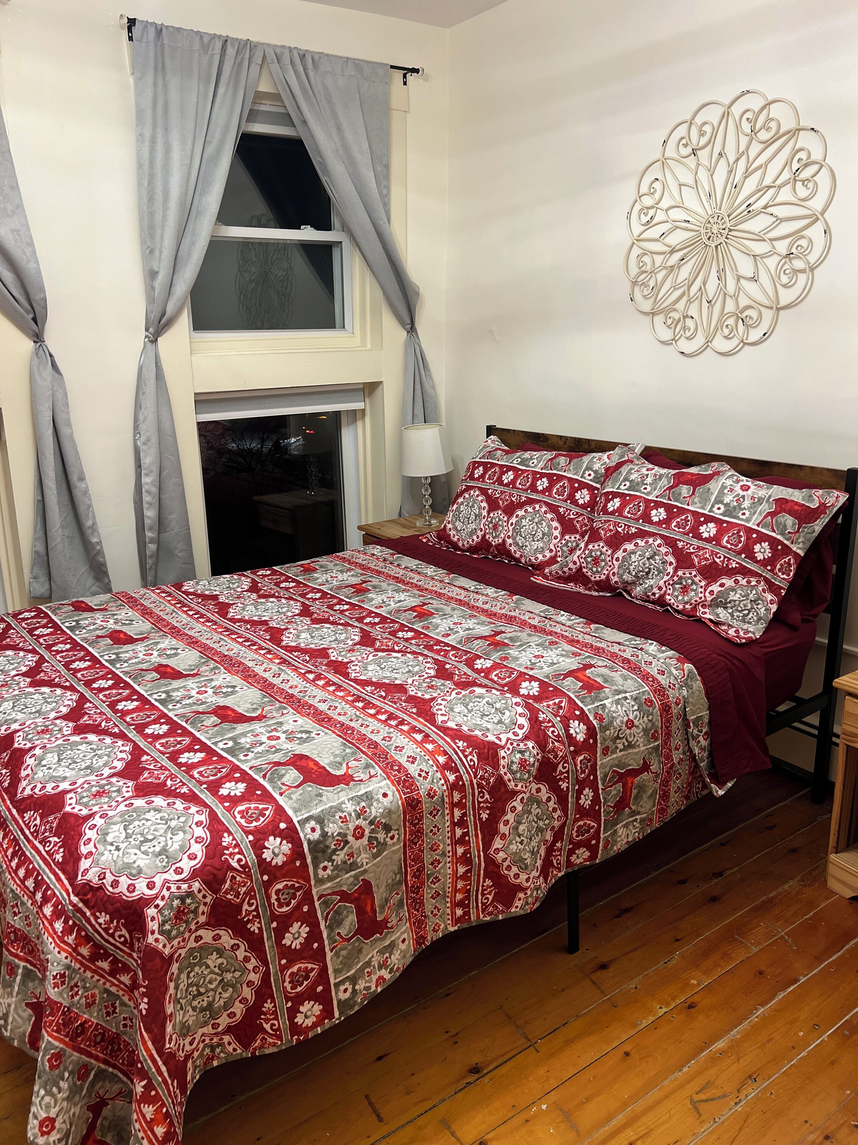 A bedroom with a large bed, grey curtains, a decorative wall piece, and a window with curtains.