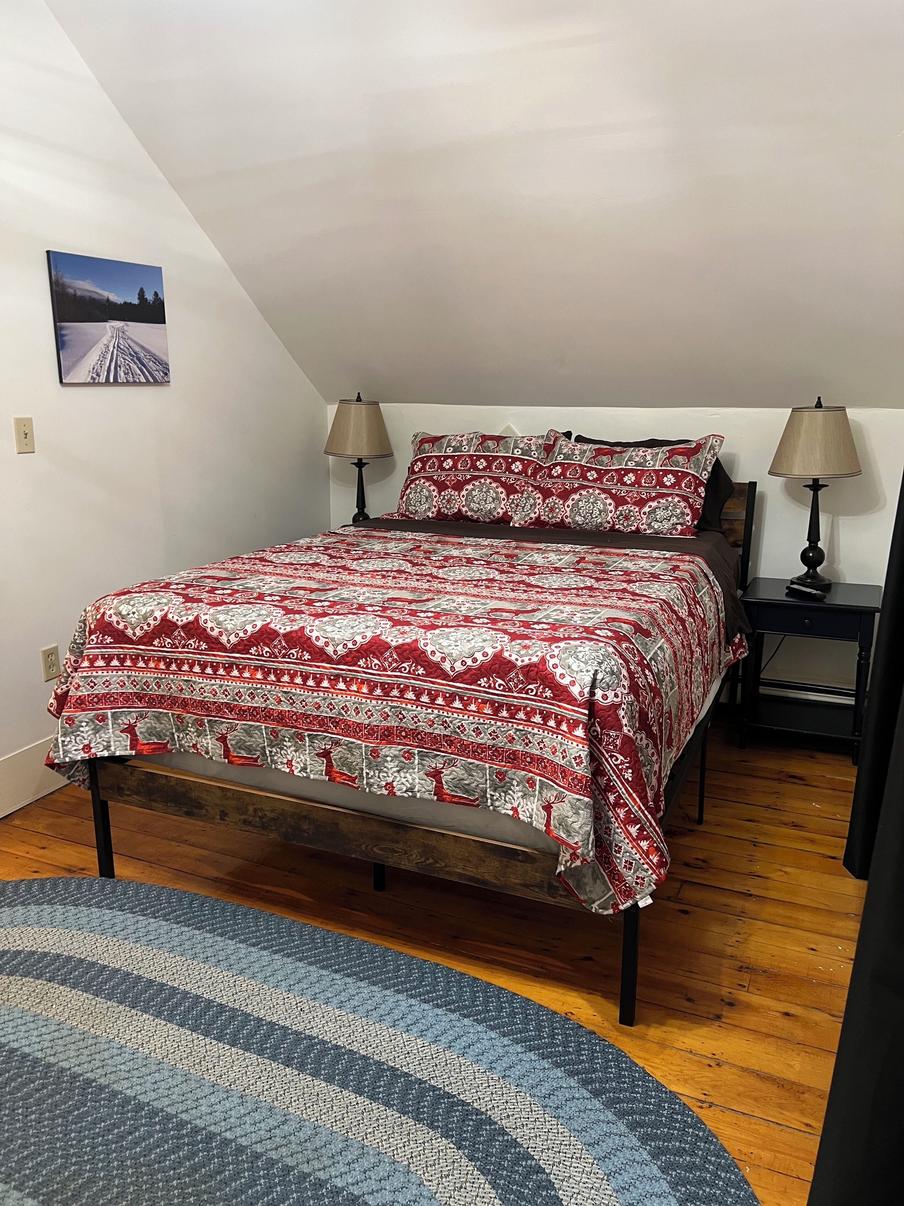 A bedroom with a bed, two bedside tables, a lamp on each table, a rug, and a picture on the wall.