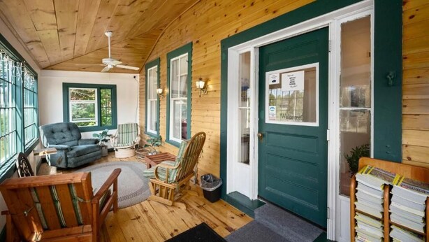 A cozy room with wooden floors, a ceiling fan, a green door, and a window with a view of greenery. - Allegory Inn (Carroll)