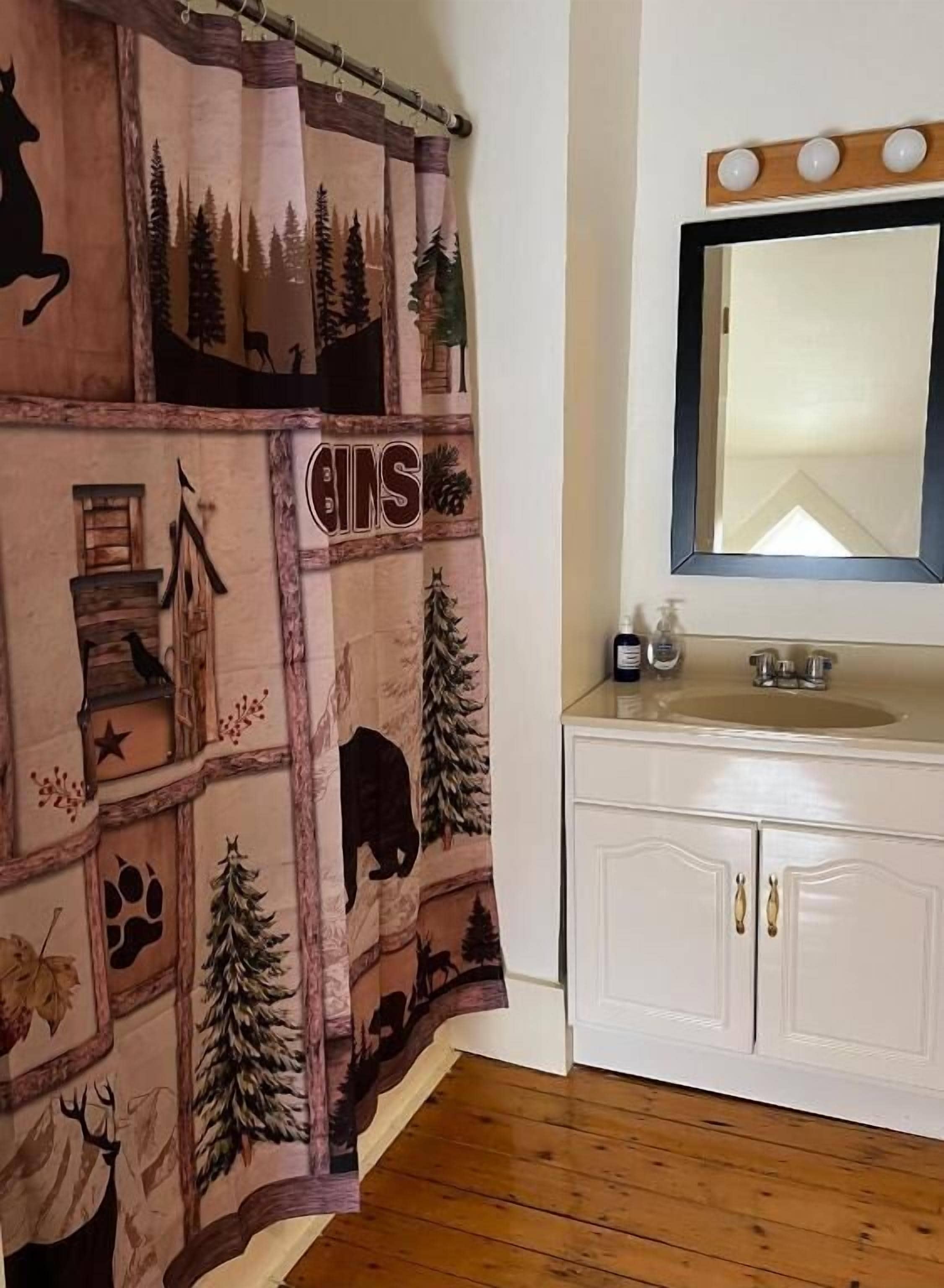 A bathroom with a wooden floor, a white sink with a mirror above it, and a shower curtain with a forest and animal print.