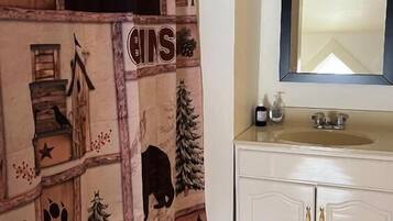 Un baño con suelo de madera, un lavamanos blanco con un espejo encima y una cortina de ducha con estampado de bosque y animales.