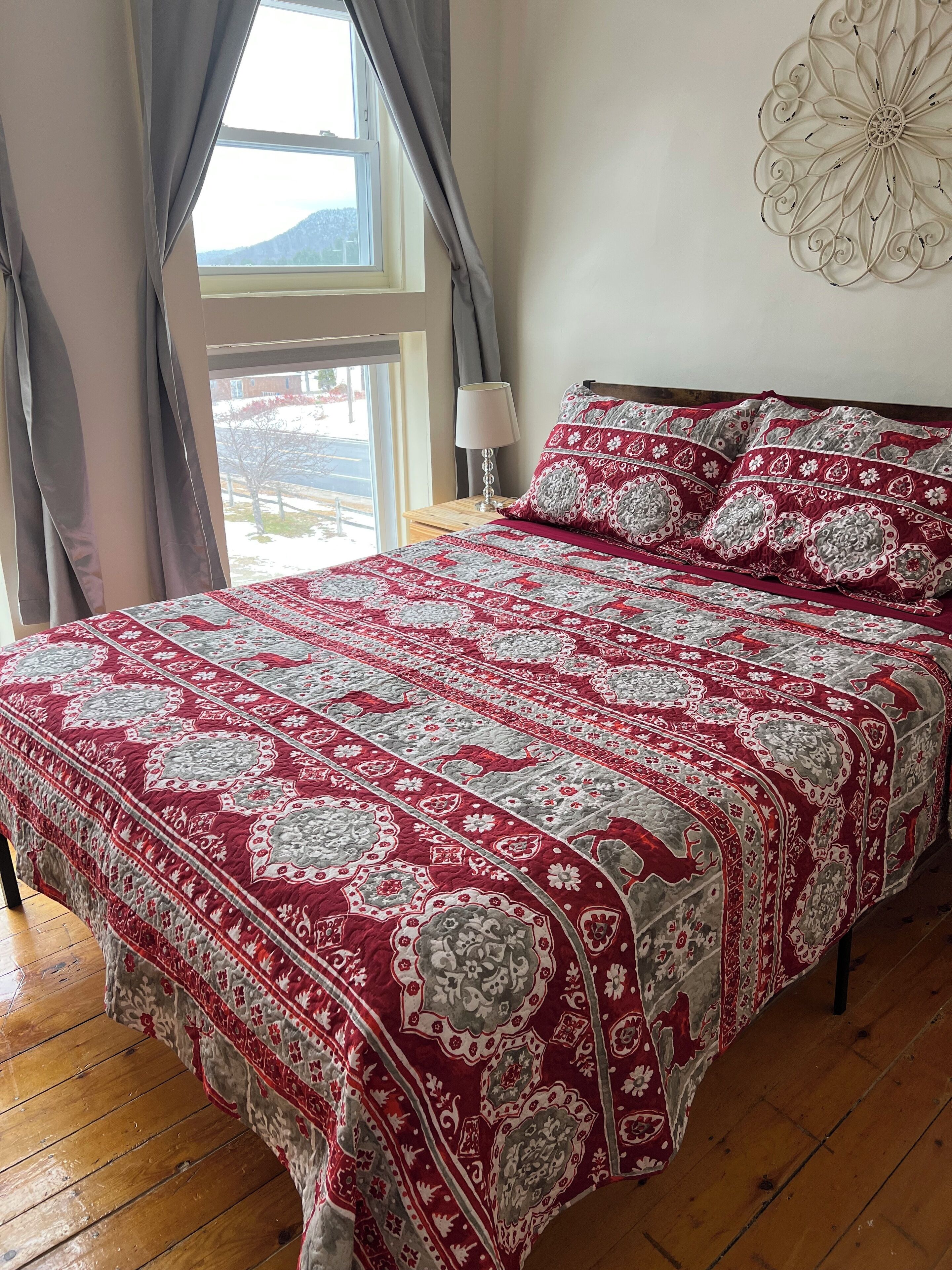 Une chambre à coucher avec un grand lit, une table de chevet avec une lampe et une fenêtre avec des rideaux.