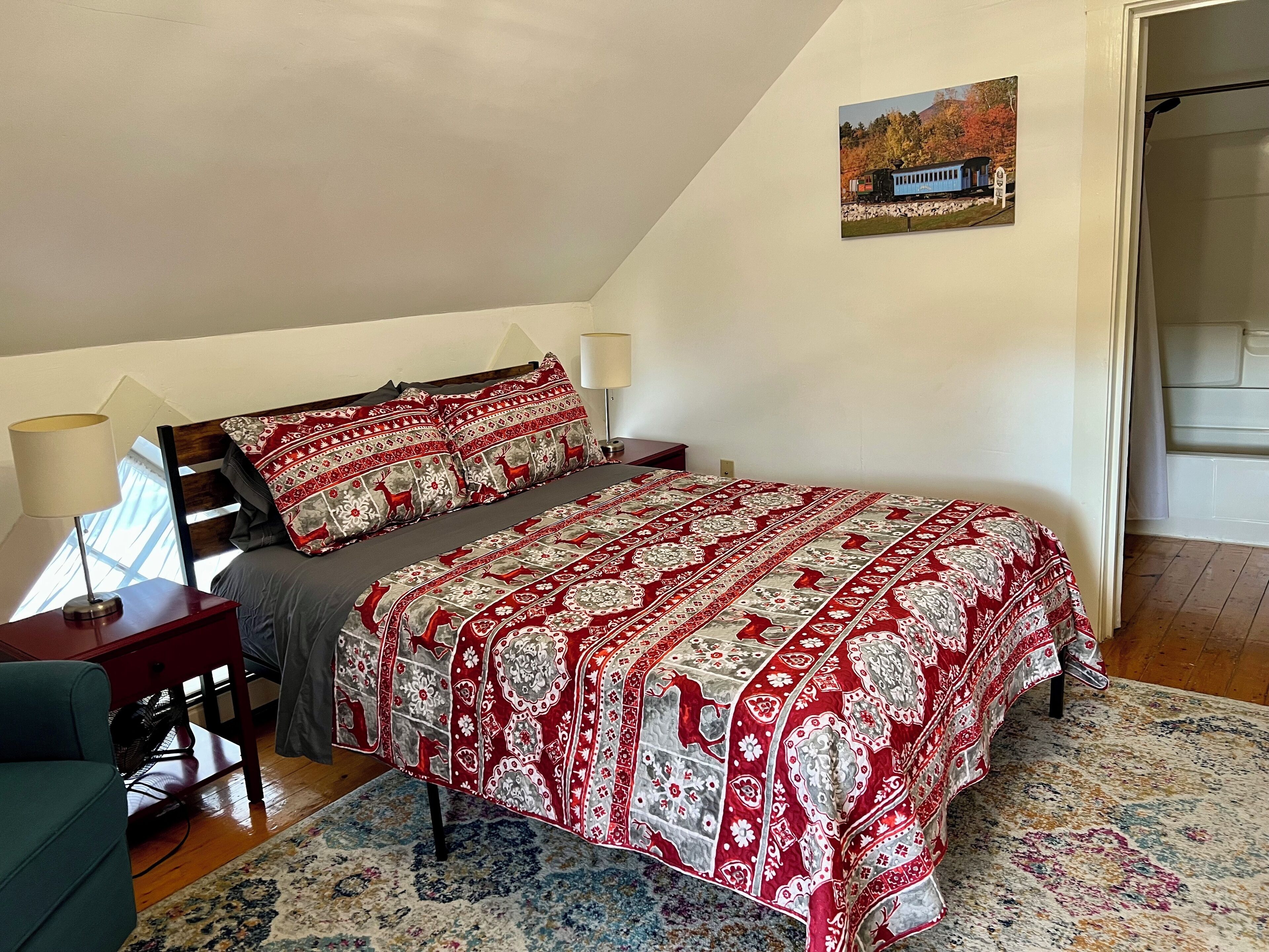 Ein Schlafzimmer mit Bett, Nachttisch, Lampe, Stuhl, Teppich und einem Gemälde an der Wand.