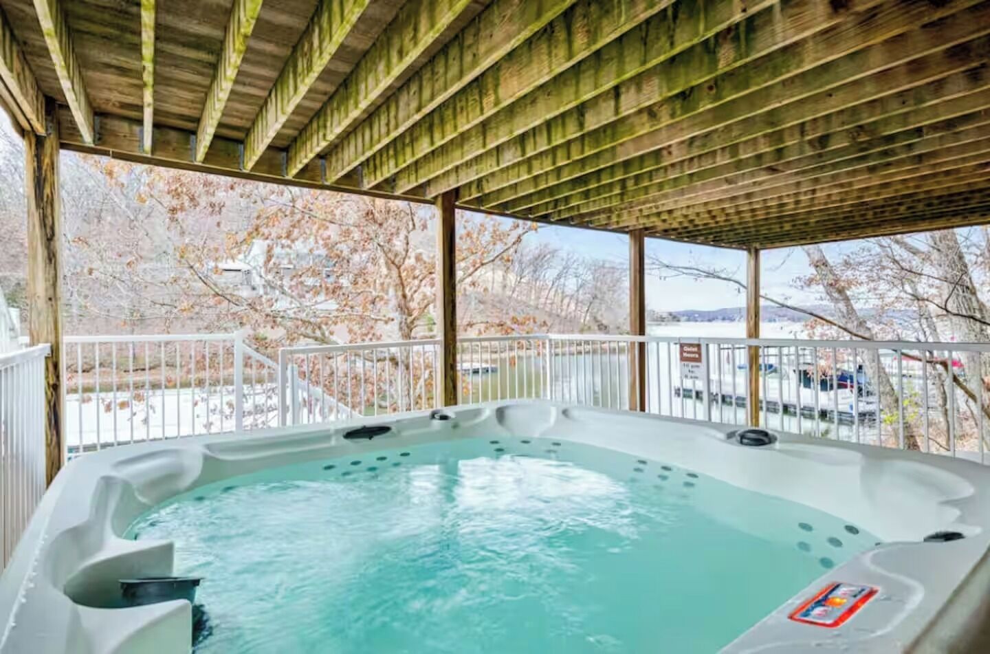Ein Whirlpool unter einer Holzpergola mit Blick auf Bäume und einen Parkplatz.