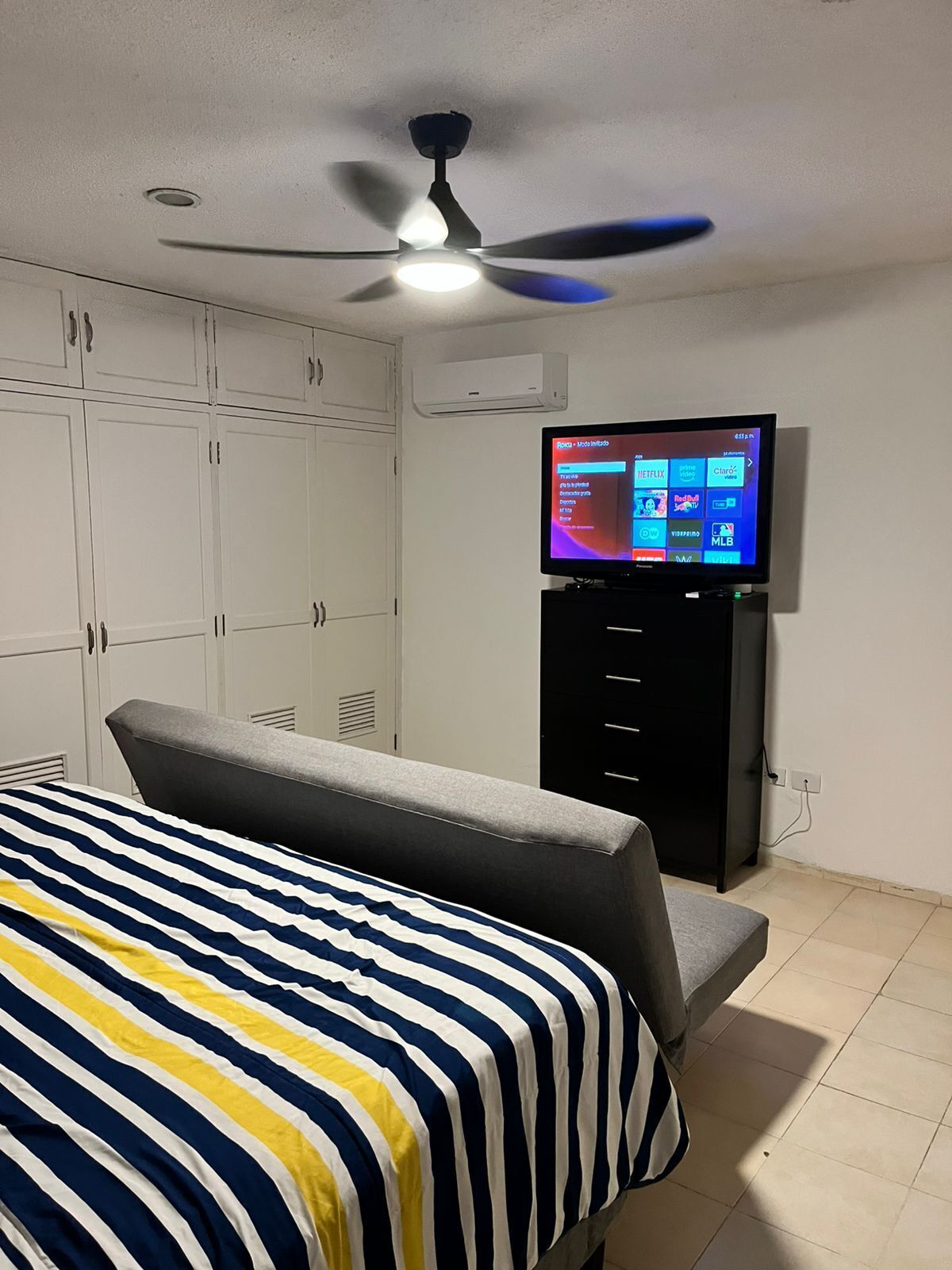 A bedroom with a bed, a TV mounted on the wall, and a ceiling fan.