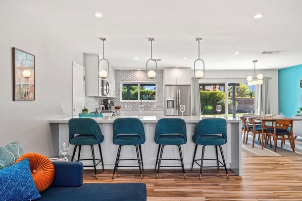 A modern kitchen with a central island, bar stools, and a dining area with wooden furniture.