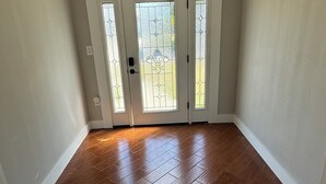 A spacious room with a wooden floor, a white door with glass panels, and a black chandelier. - Waterfront Home w dock & pool table 3 bedroom, sleeps 8 (Bradenton)