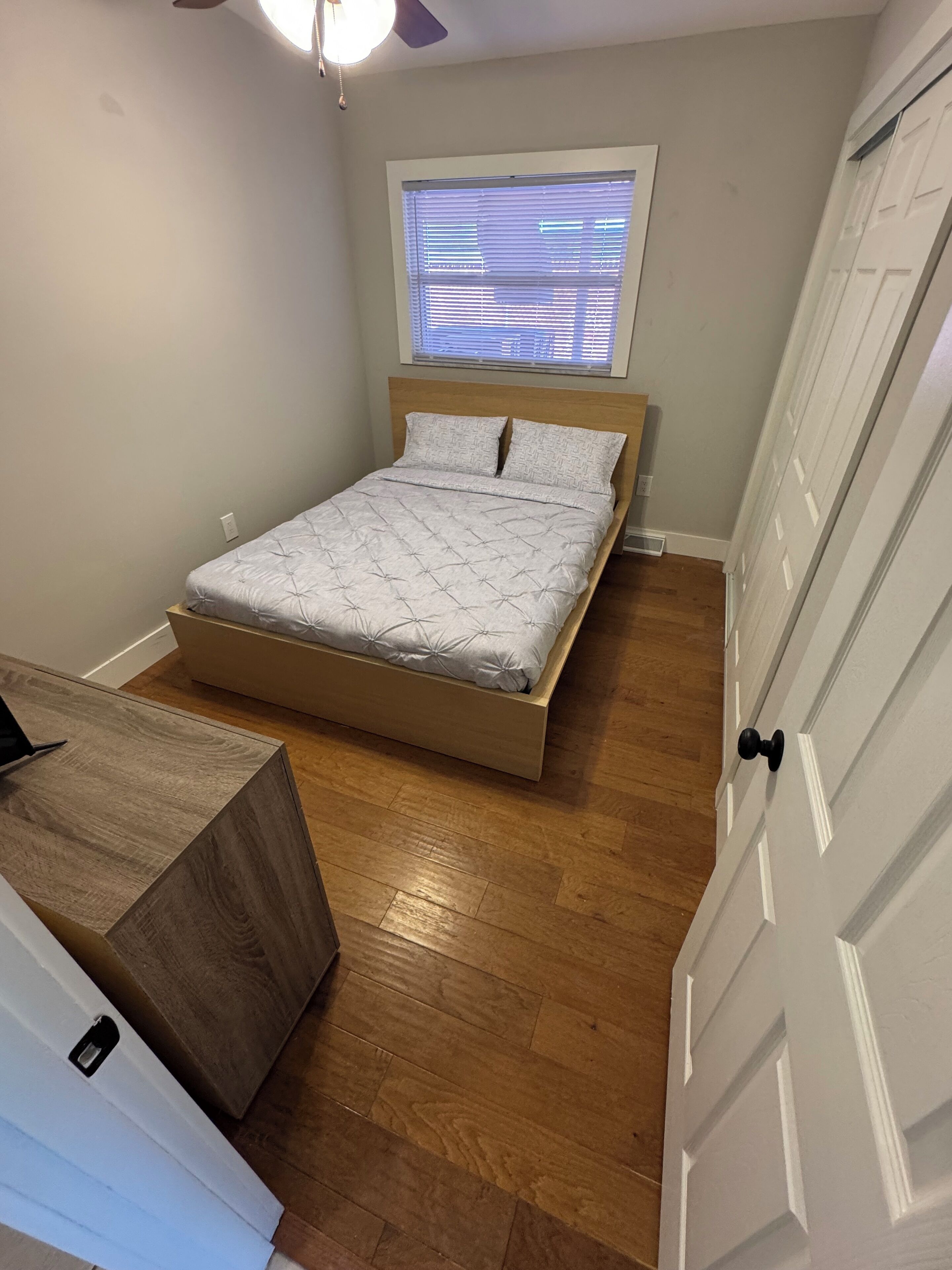 Un dormitorio pequeño con una cama, un escritorio de madera y una ventana con persianas.