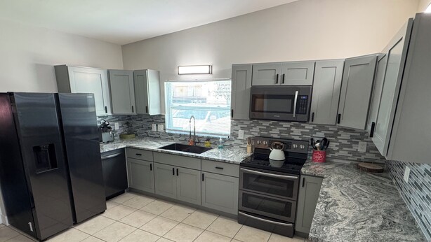 A kitchen with grey cabinets, a black refrigerator, a microwave, a stove, and a sink. - Waterfront Home w dock & pool table 3 bedroom, sleeps 8 (Bradenton)