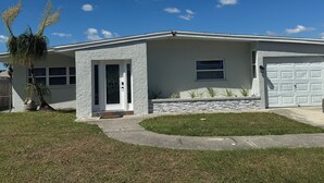 A single-story house with a white exterior, a front door with a glass panel, a garage door, and a small window. - Waterfront Home w dock & pool table 3 bedroom, sleeps 8 (Bradenton)