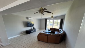 A spacious living room with a sectional sofa, a flat-screen TV, a ceiling fan, and a large window providing natural light. - Waterfront Home w dock & pool table 3 bedroom, sleeps 8 (Bradenton)