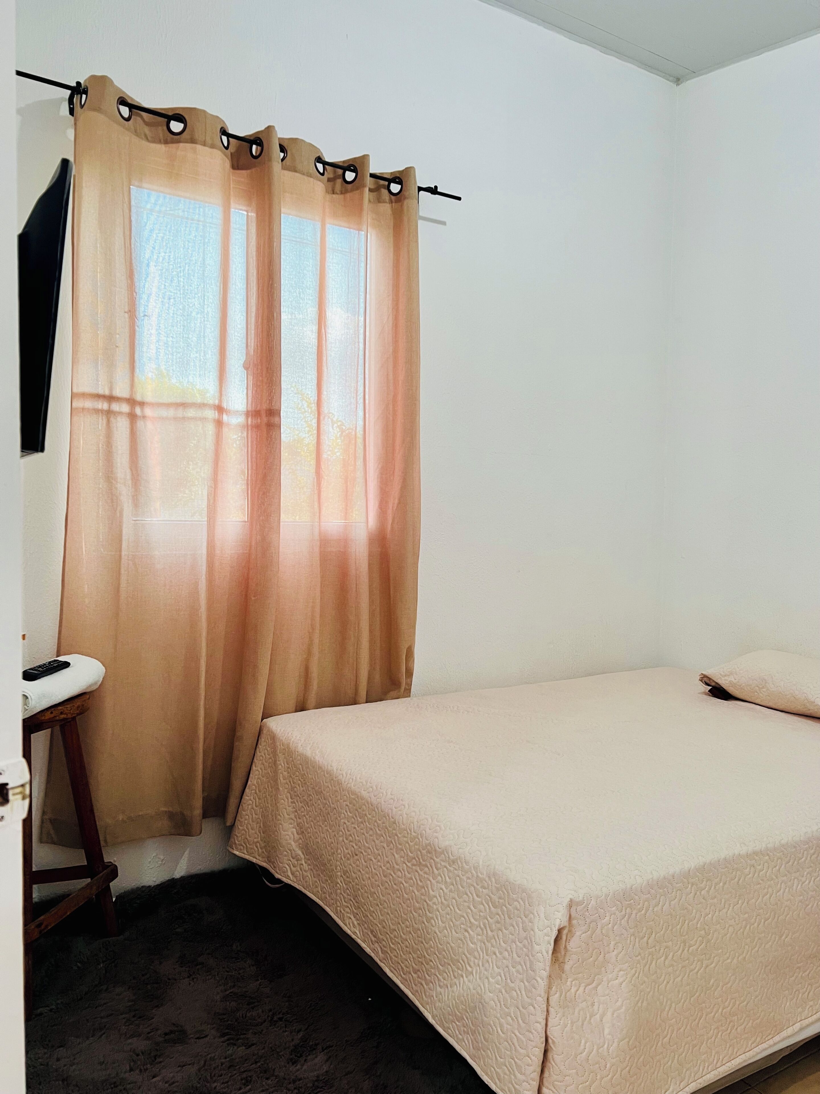 Een slaapkamer met een bed, een stoel, een bureau en een raam met gordijnen.