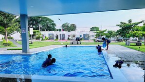 A swimming pool with people in the water, surrounded by a covered area with a view of residential buildings. - Nala House  (Nuevo Sitio del Nino)