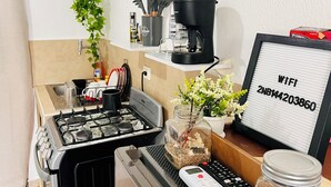 A kitchen with a gas stove, a coffee maker, a WiFi sign, a jar with a plant, and a remote control. - Nala House  (Nuevo Sitio del Nino)
