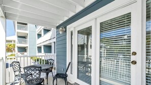 Un espace extérieur abrité, doté d’une table et de chaises, d’une porte avec une fenêtre et d’un balcon pourvu de balustrades.
