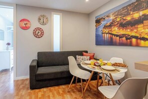 Uma sala de estar moderna com um sofá escuro, cadeiras brancas, uma mesa de jantar com café da manhã e três relógios na parede.