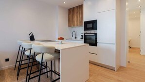 Une cuisine moderne avec des meubles blancs, un îlot central doté de tabourets, un four à micro-ondes et un four traditionnel.