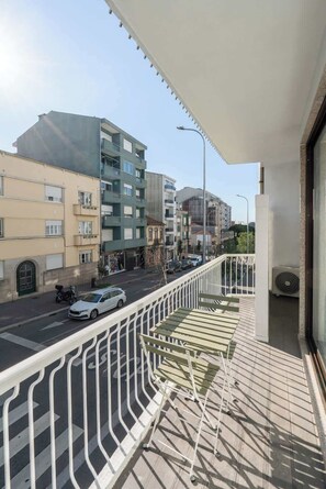A balcony with a metal railing overlooking a street with cars and buildings.