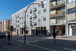 A multi-story residential building with balconies, a pedestrian crossing, and a street with parked motorcycles.